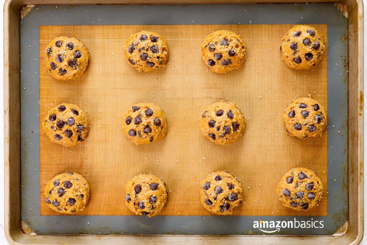 showing how to make pumpkin chocolate chip cookies by placing cookie dough balls on a baking sheet