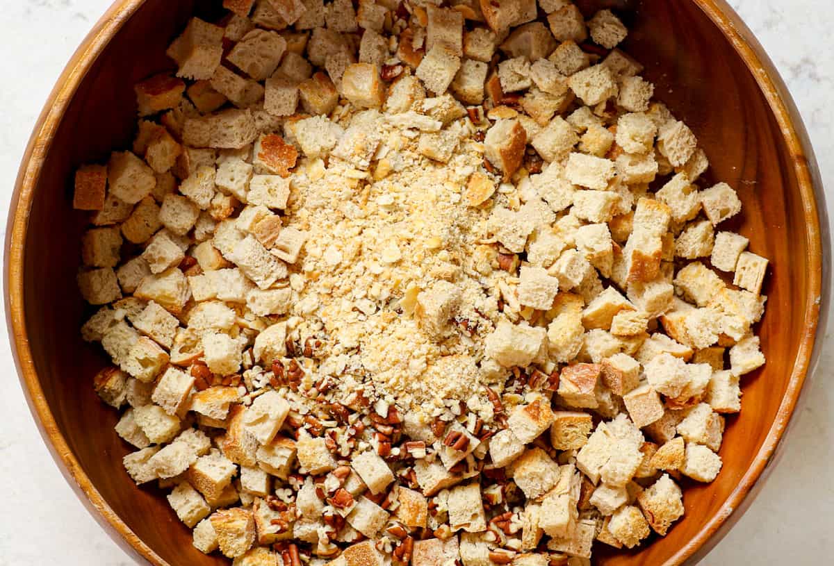 showing how to make stuffing by adding toasted bread cubes to a bowl with pecans and cracker crumbs