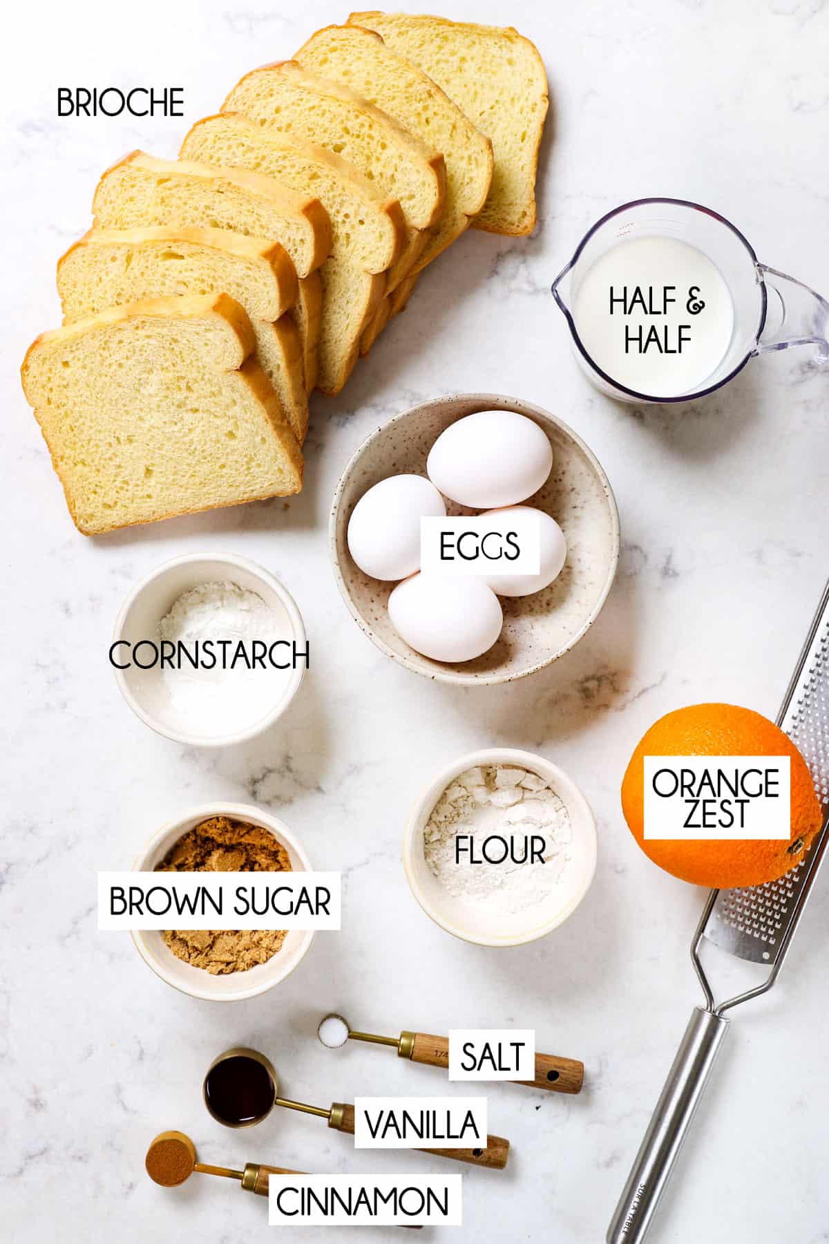 showing ingredients for French toast lined up:  brioche bread, eggs, half and half, flour, vanilla extract, salt, nutmeg and orange zest