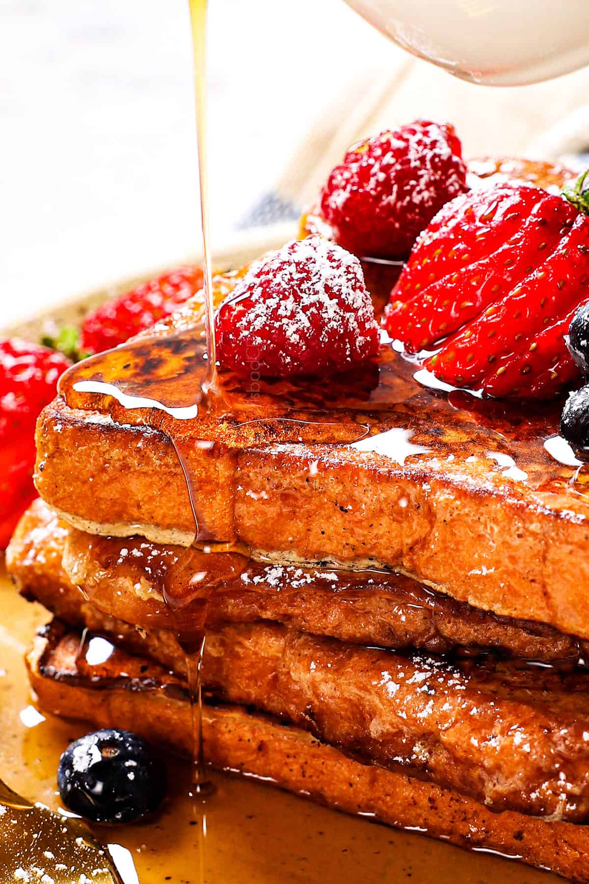 showing how to serve easy french toast by dusting with powdered sugar, topping with syrup and berries