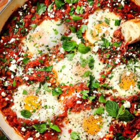 showing how to make shakshuka by garnishing with feta, cilantro and parsley