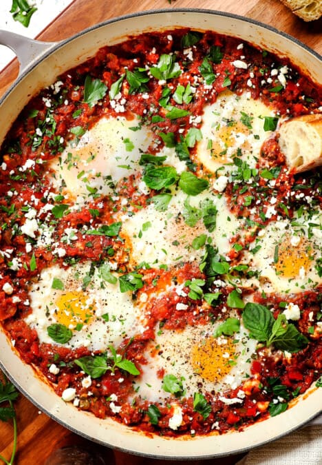 showing how to make shakshuka by garnishing with feta, cilantro and parsley
