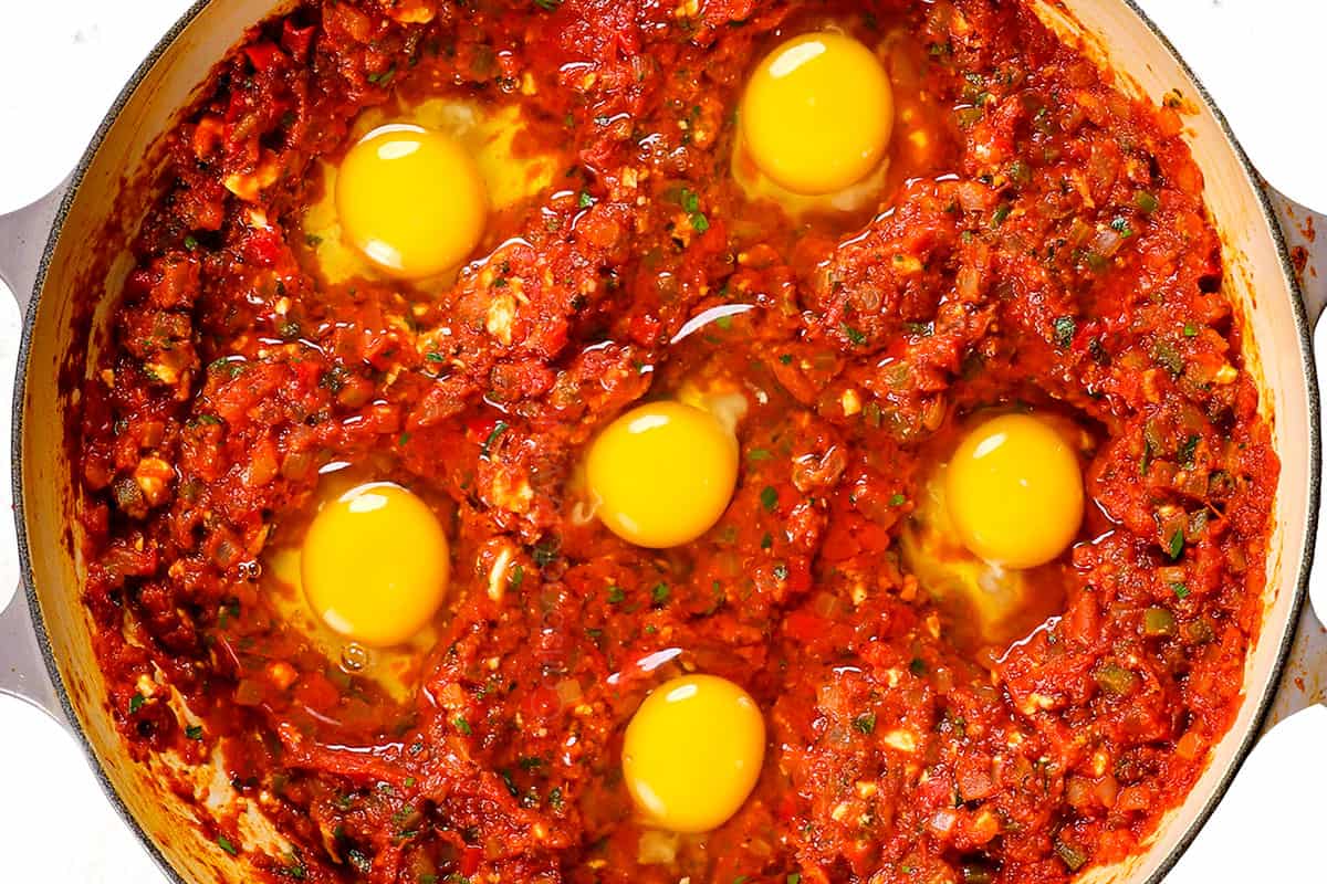 showing how to make shakshuka by adding eggs to tomato bell pepper sauce to poach