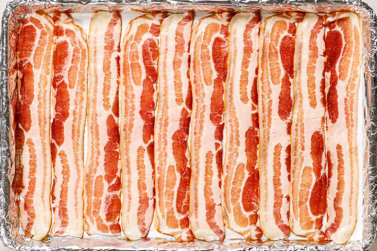 showing how to cook bacon in the oven by lining raw bacon in a single layer in a parchment lined baking sheet
