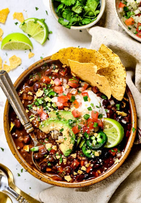 showing how to serve black bean soup recipe in a bowl with sour cream, avocados, jalapenos and pic de gallo