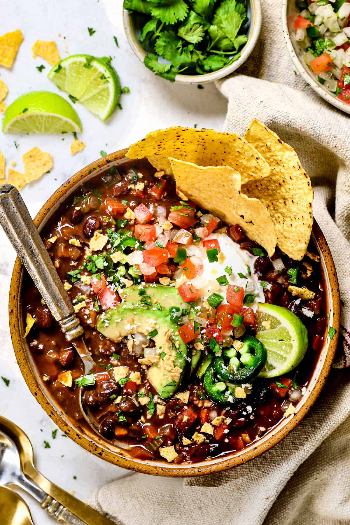 showing how to serve black bean soup recipe in a bowl with sour cream, avocados, jalapenos and pic de gallo