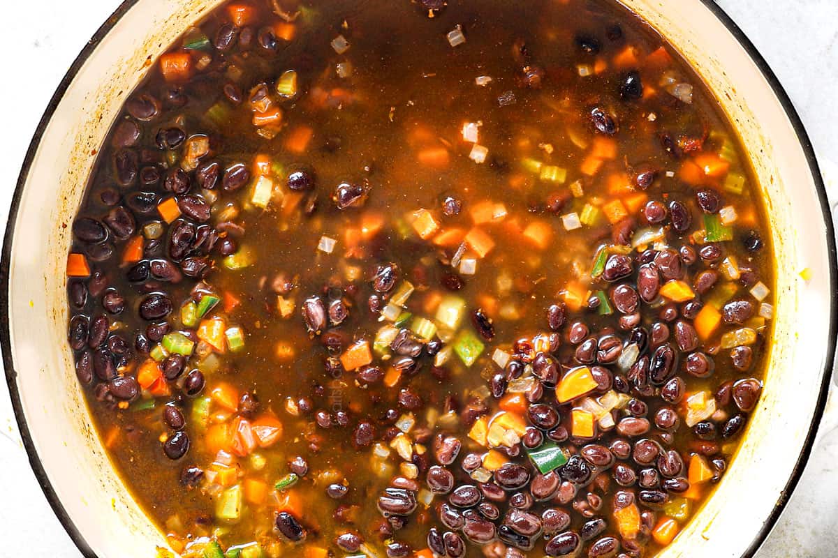 showing how to make black bean soup by adding beans and vegetable broth and simmering soup 