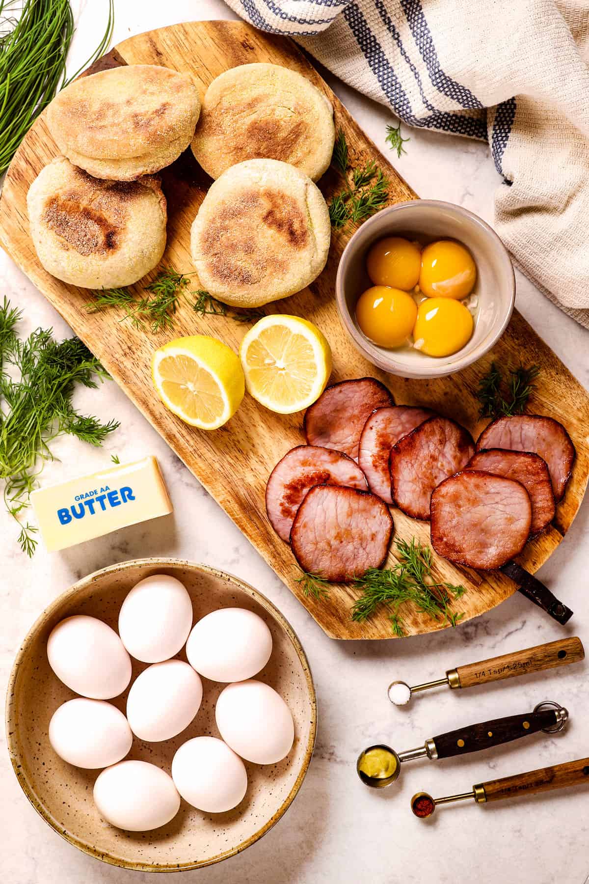 top view showing ingredients to make Eggs Benedict: eggs, Canadian bacon, English Muffins, egg yolks and butter