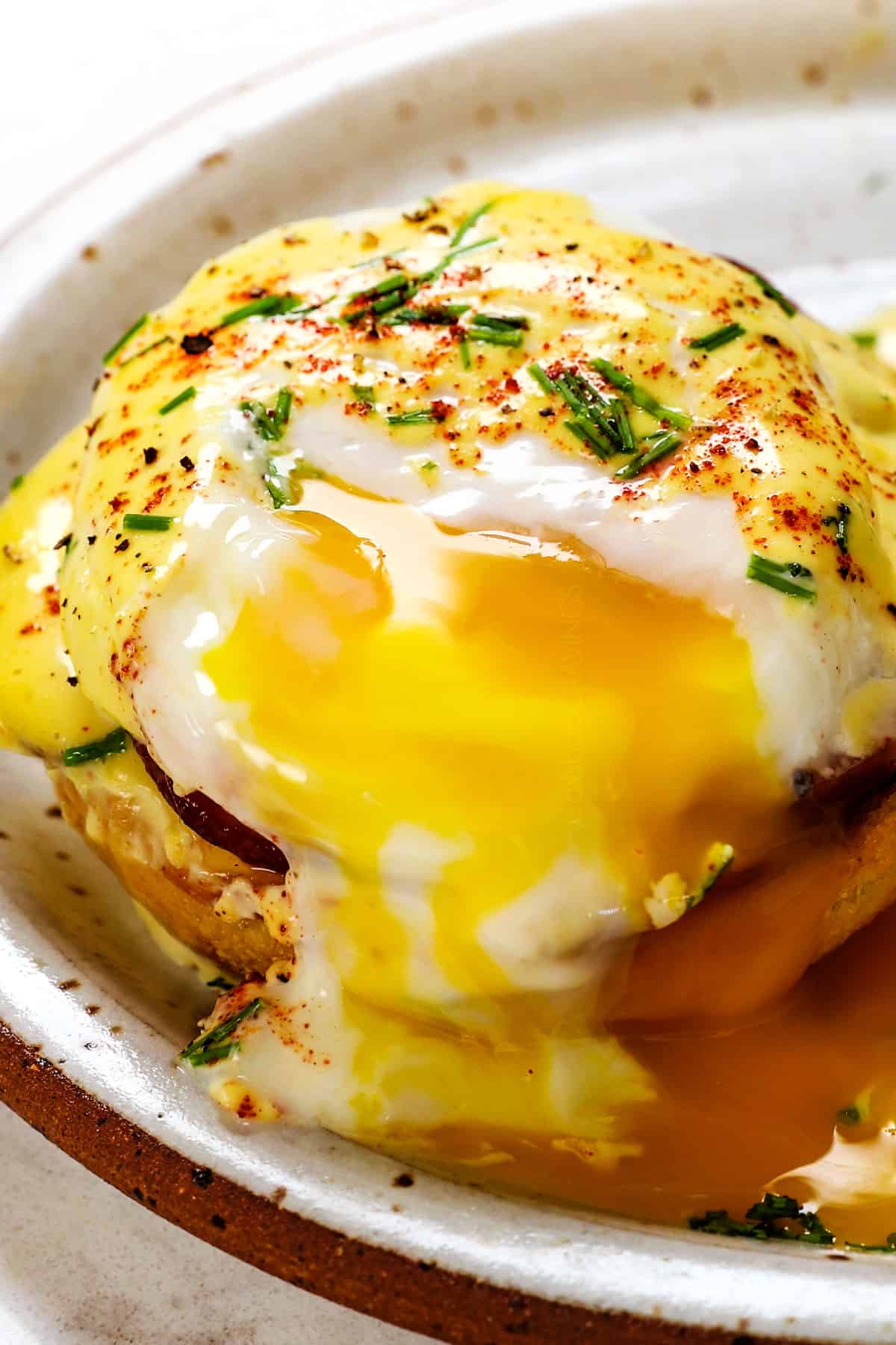 up close of egg benedict recipe with the yolk running on the plate