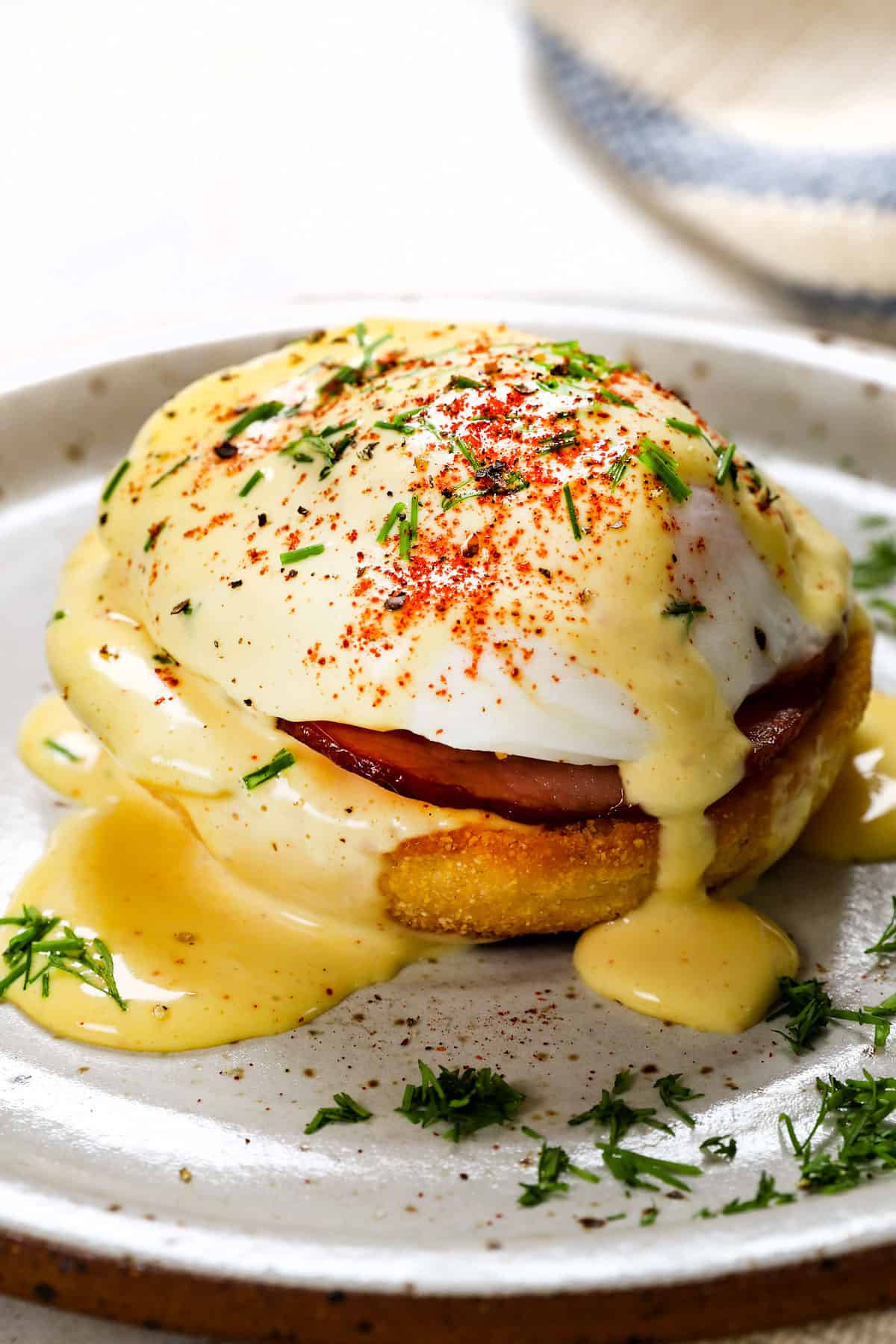 showing how to make Eggs Benedict recipe by assembling with English Muffin, Canadian Bacon, poached egg and hollandaise sauce