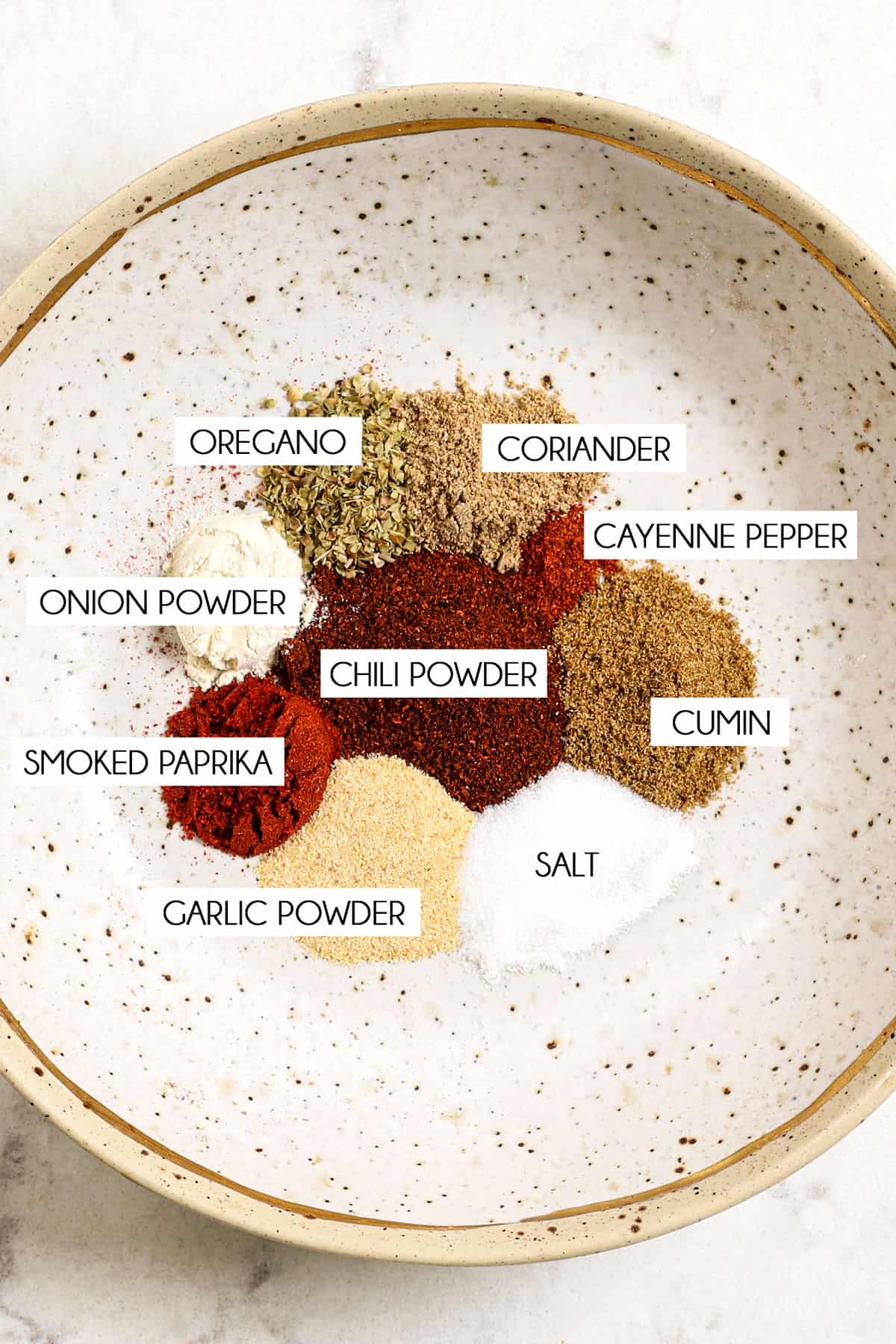 showing how to make taco seasoning by adding chili powder, cumin, smoked paprika, oregano, garlic powder, onion powder and cayenne to a bowl