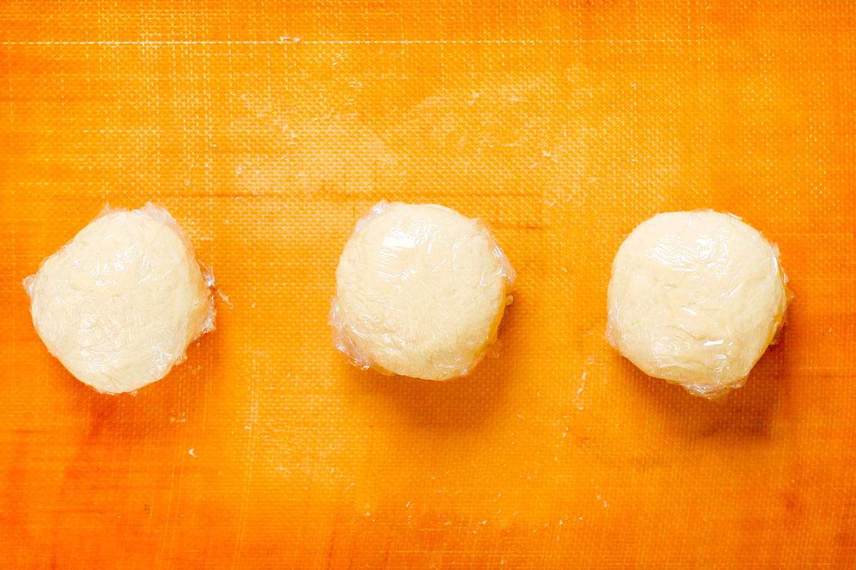 showing how to make pierogi by dividing pierogi dough into three balls and wrapping in plastic wrap