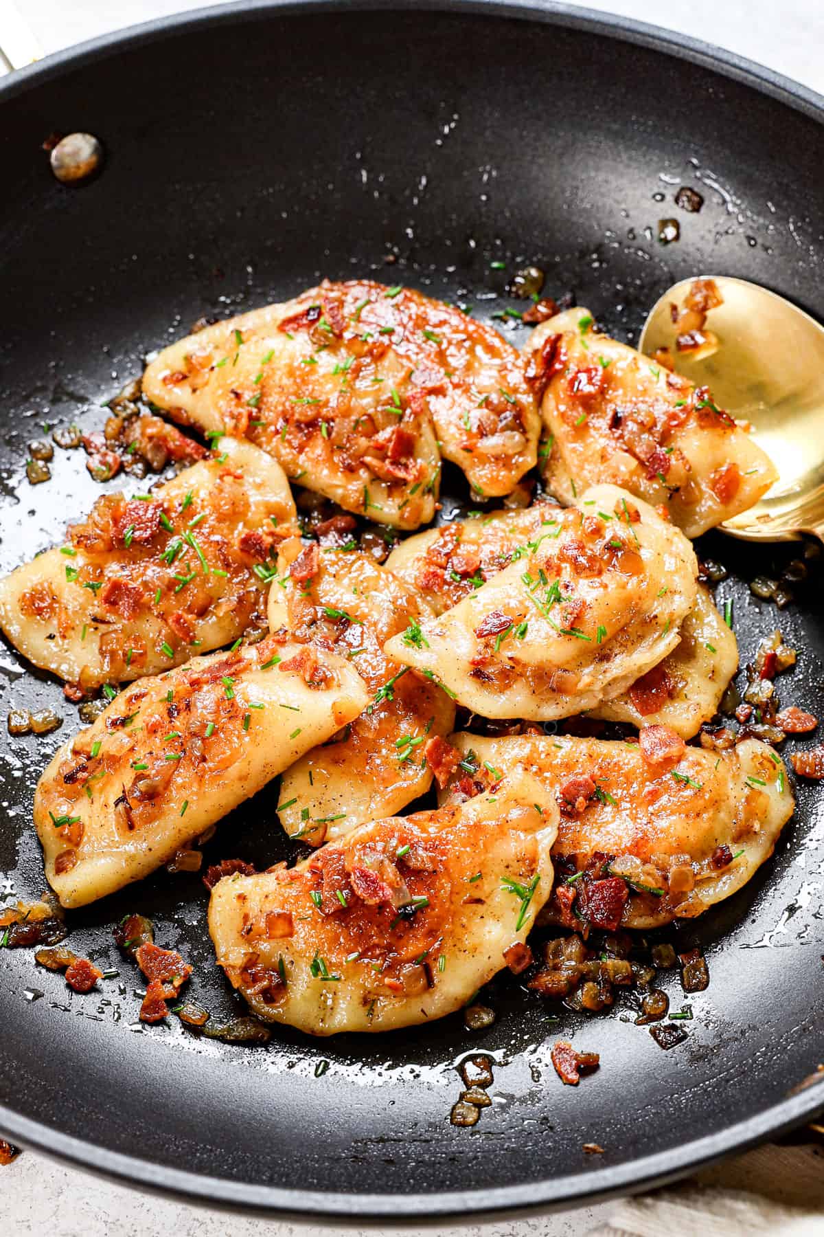homemade pierogi recipe in a nonstick skillet garnished with green onions 