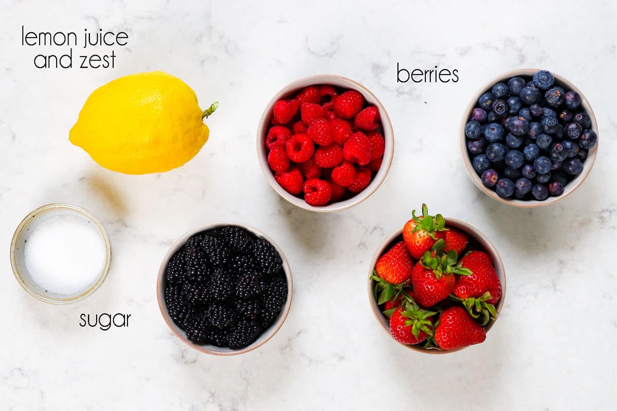 top view showing ingredients for Chantilly Cake berry filling: strawberries, raspberries, blackberries, blueberries, sugar, lemon juice and lemon zest
