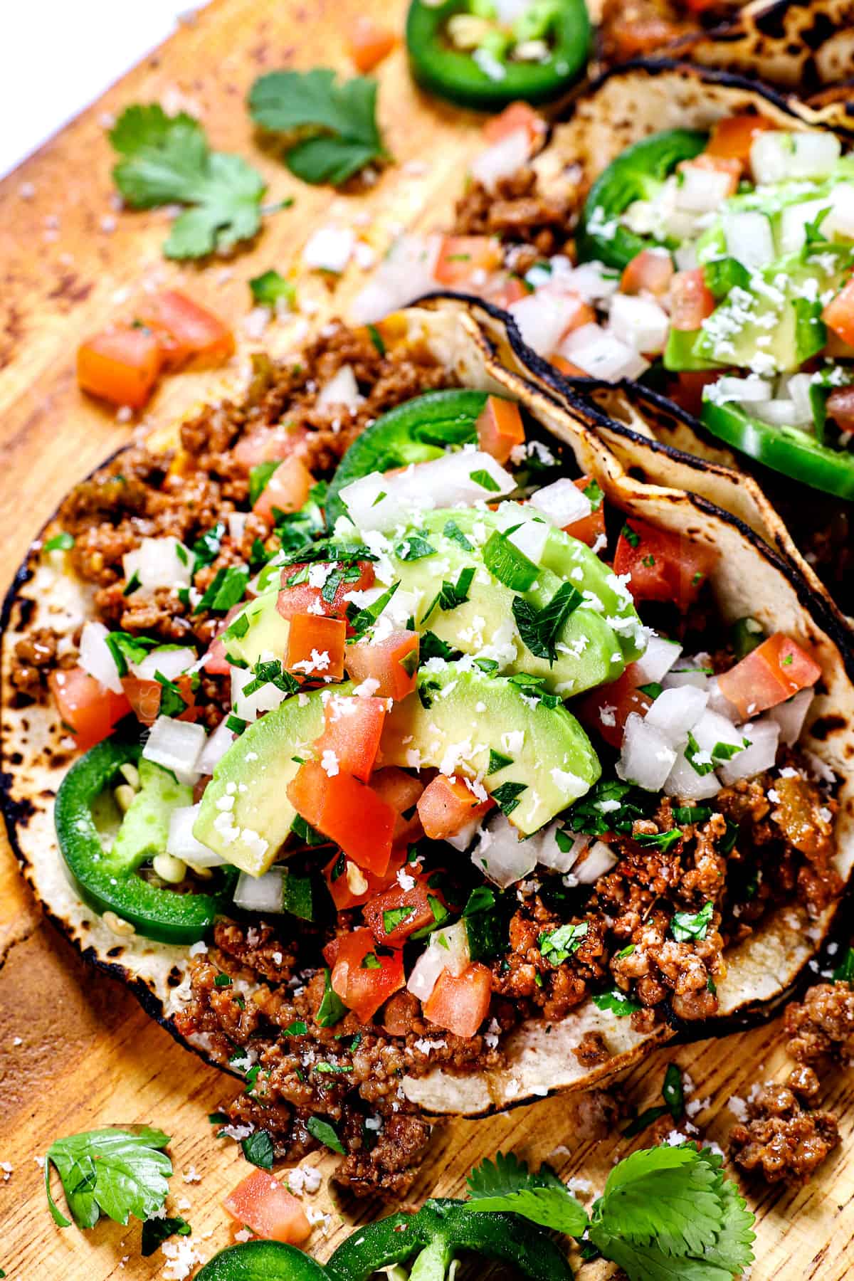 showing how to serve taco meat in a taco shell with avocados, tomatoes and cilantro