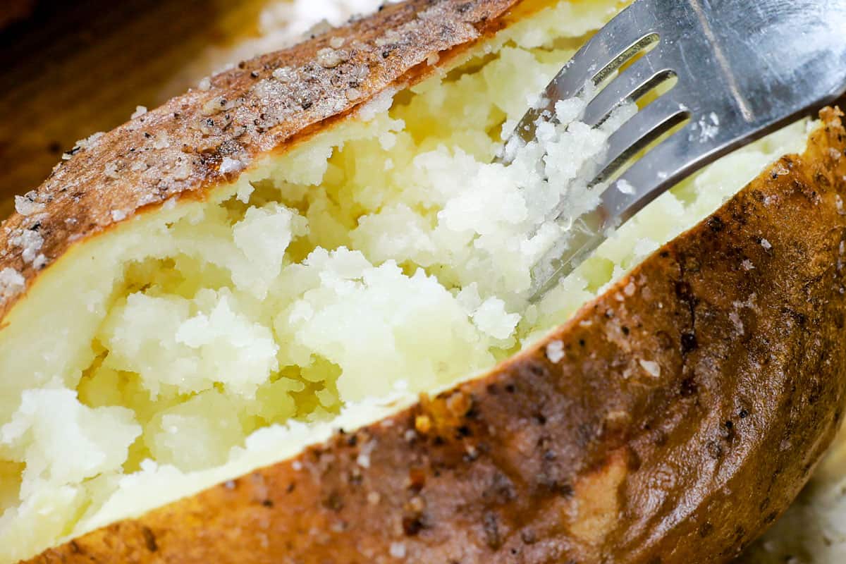 showing how to make a baked potato in the oven by fluffing potato inside with a fork