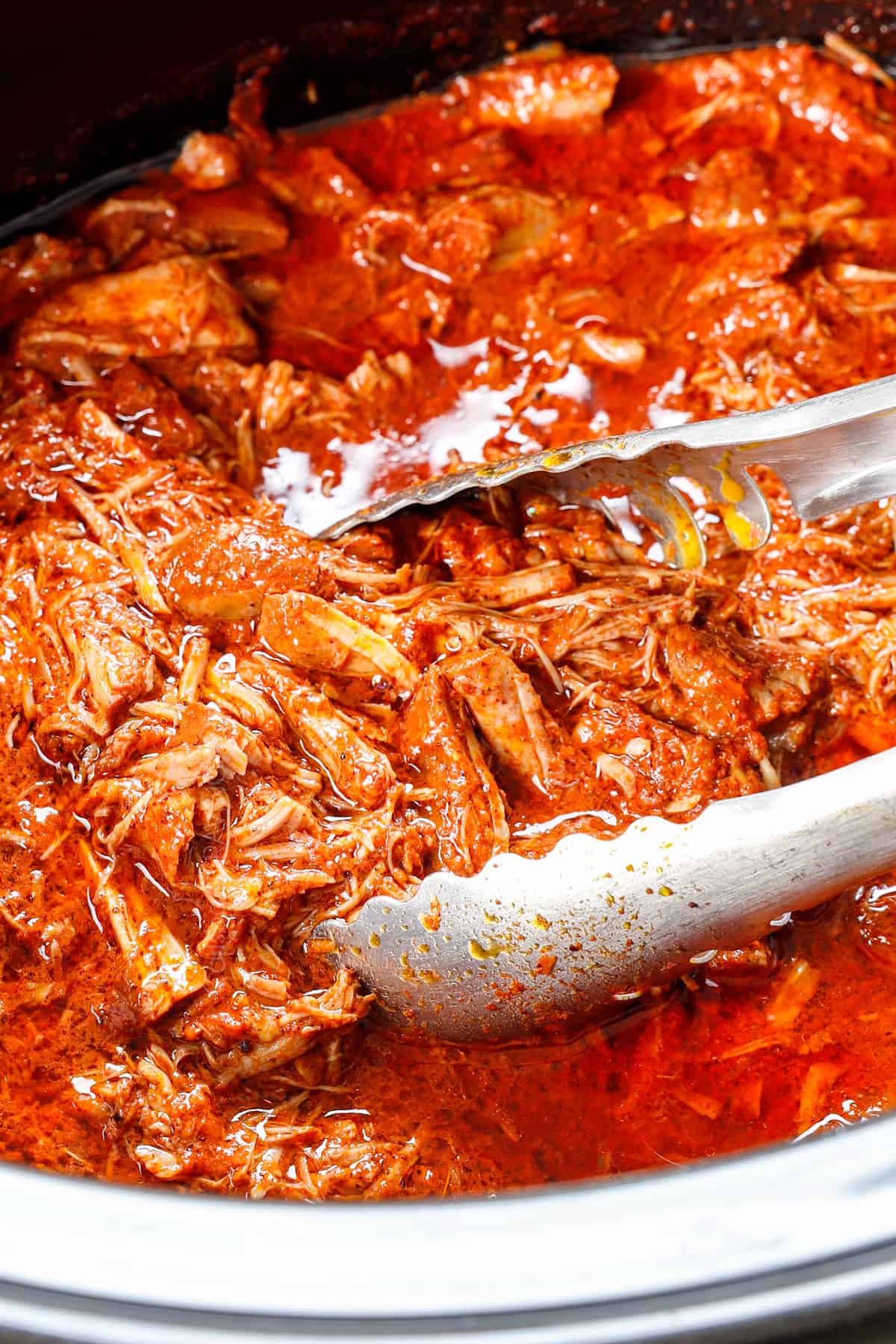 showing how to make cochinita pibil by straining the pork from the juices with tongs