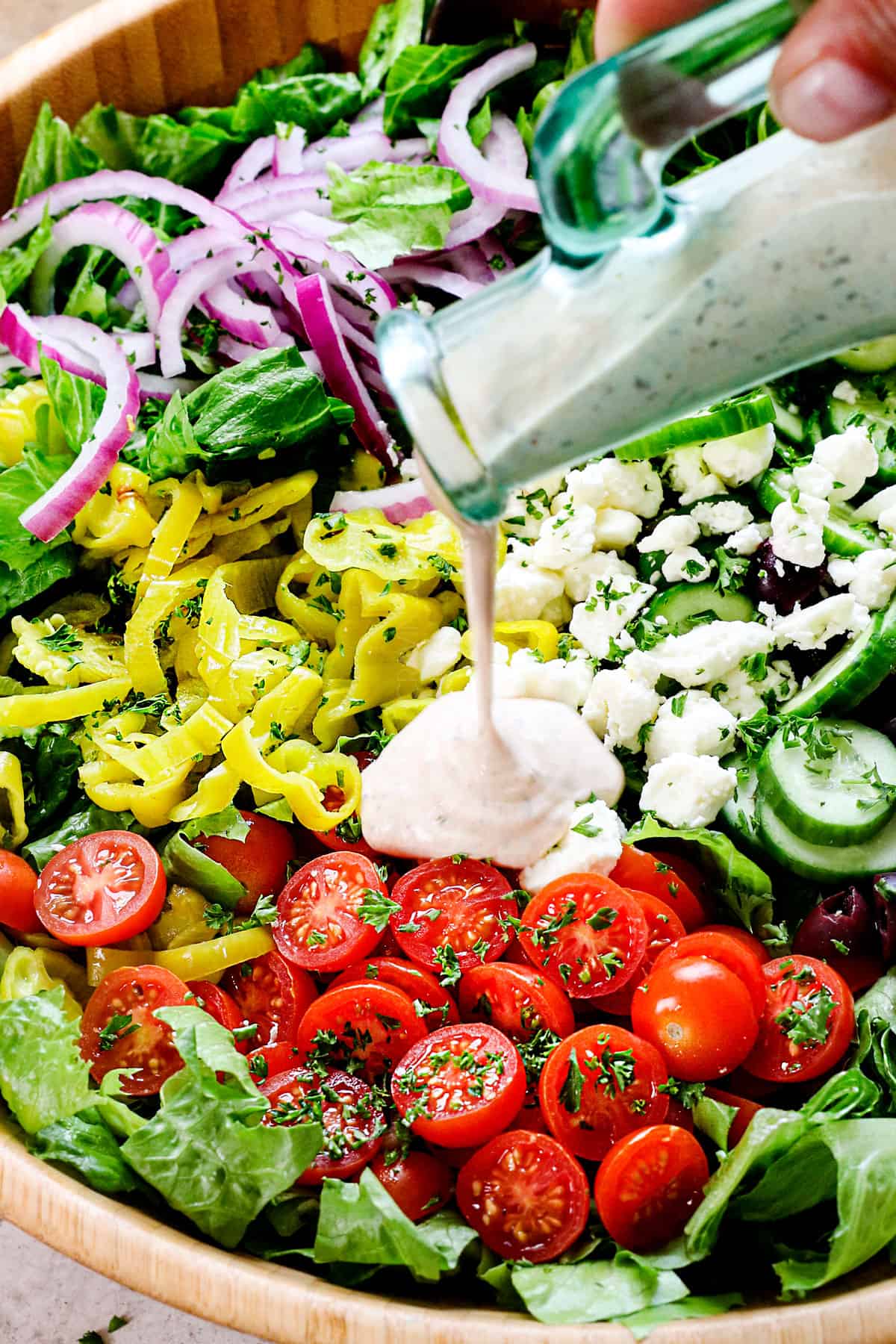 showing how to make Mediterranean salad by pouring the dressing over the salad