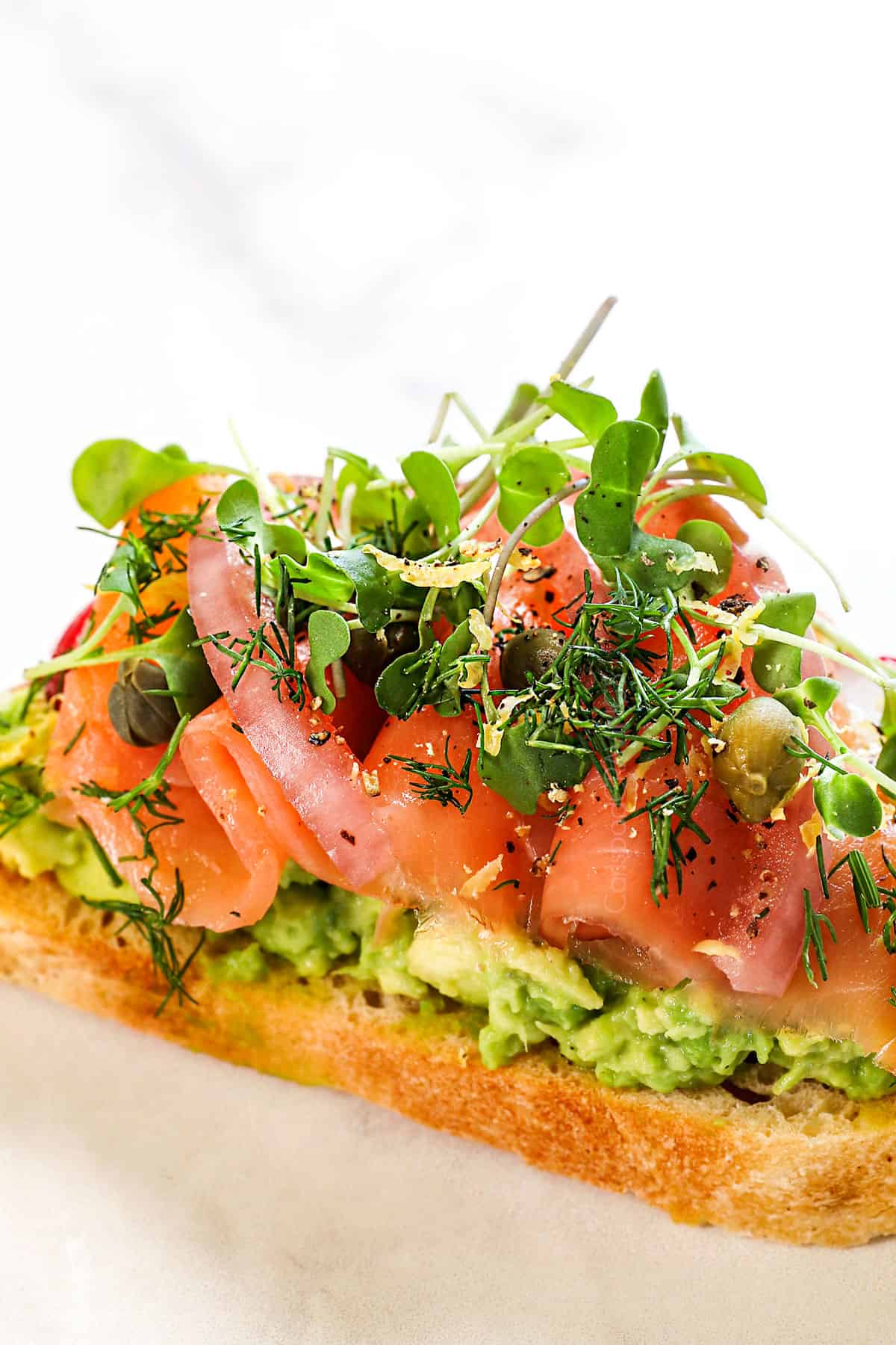 showing variation of avocado toast with toppings of smoked salmon, pickled red onions and microgreens