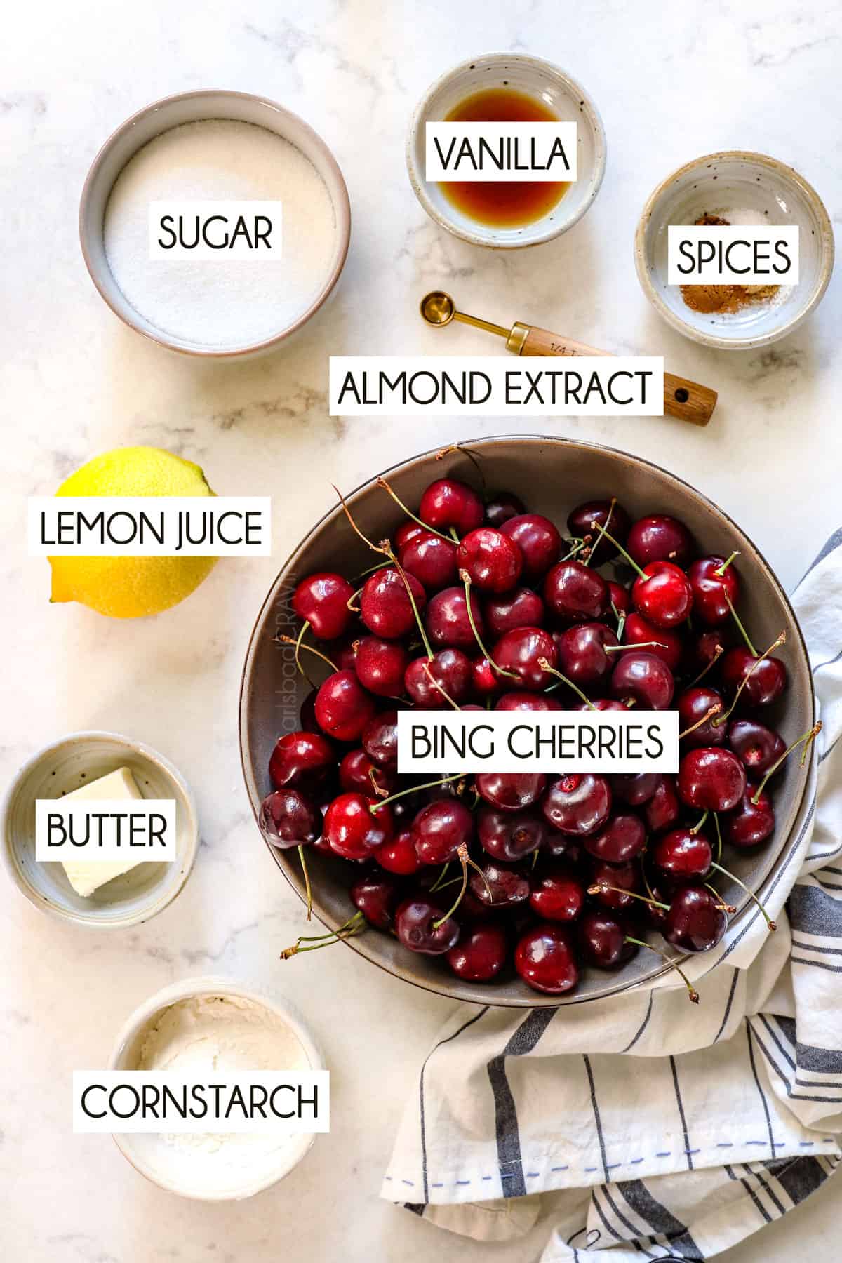 top view of cherry pie ingredients: sweet cherries, sugar, lemon juice, vanilla extract, almond extract, cornstarch, spices