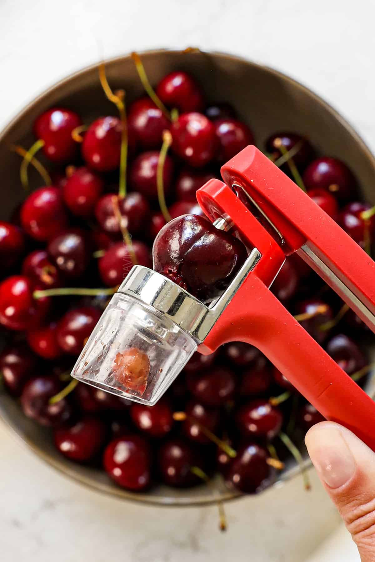 showing how to make cherry pie recipe by pitting a cherry with a cherry pitter