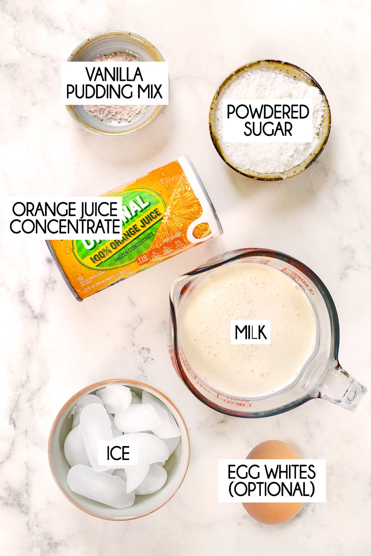 top view showing ingredients for orange Julius: orange juice concentrate, sugar, milk, vanilla, ice cubes and egg white