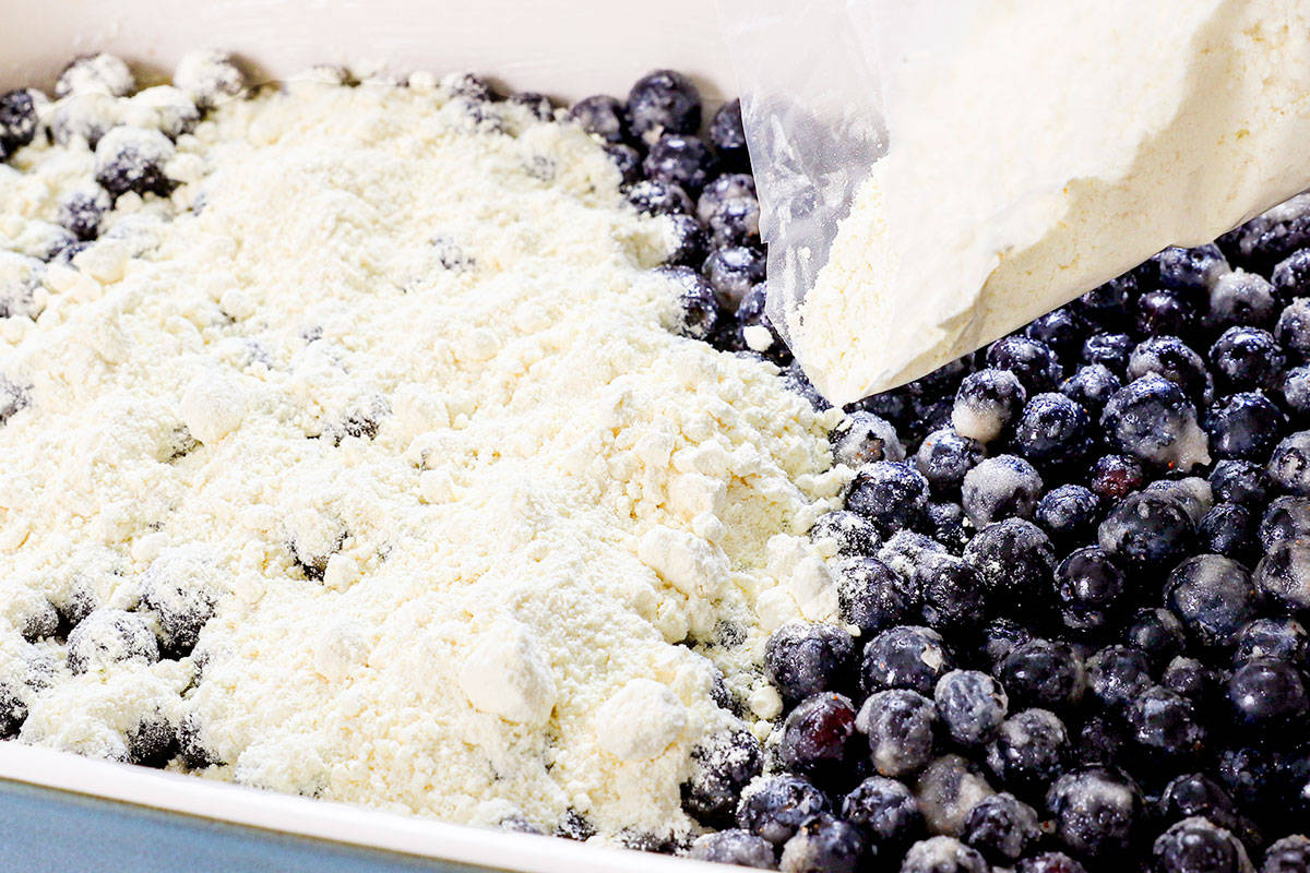 showing how to make a blueberry dump cake by sprinkling the cake mix over the blueberries