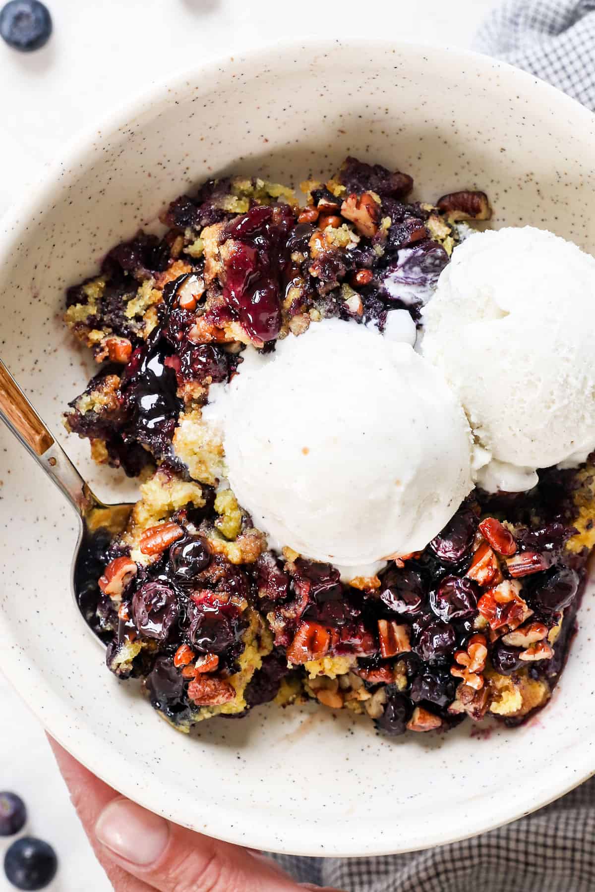 holding a bowls with blueberry dump cake topped with ice cream showing how to serve