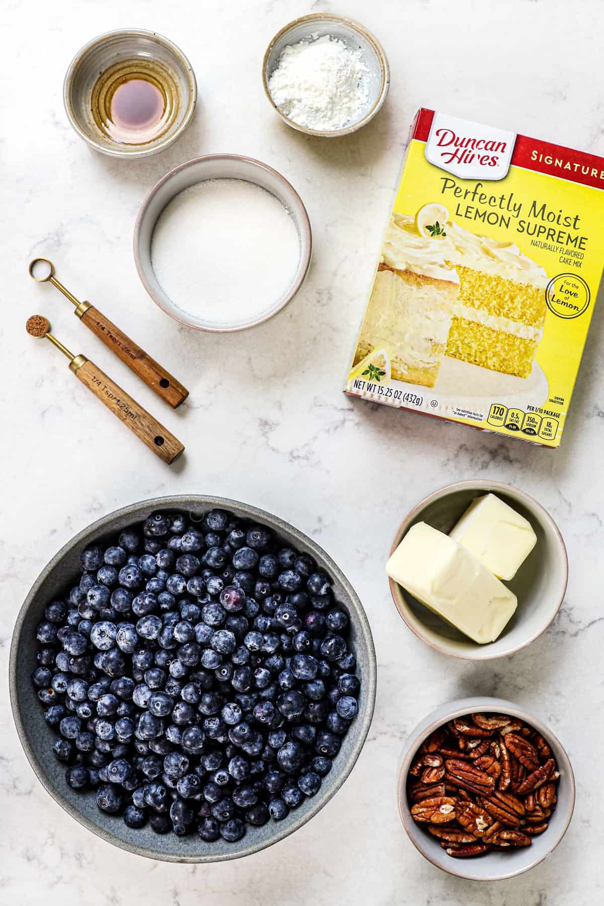 top view of ingredients for blueberry dump cake:  blueberries, butter, pecans, cornstarch, sugar, vanilla and lemon cake mix