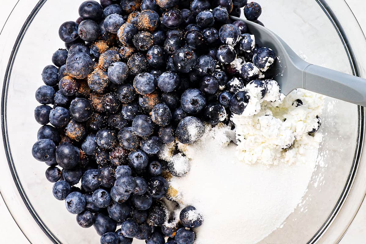 showing how to make a blueberry dump cake by combining the blueberries, sugar, cornstarch, vanilla and seasonings in a bowl