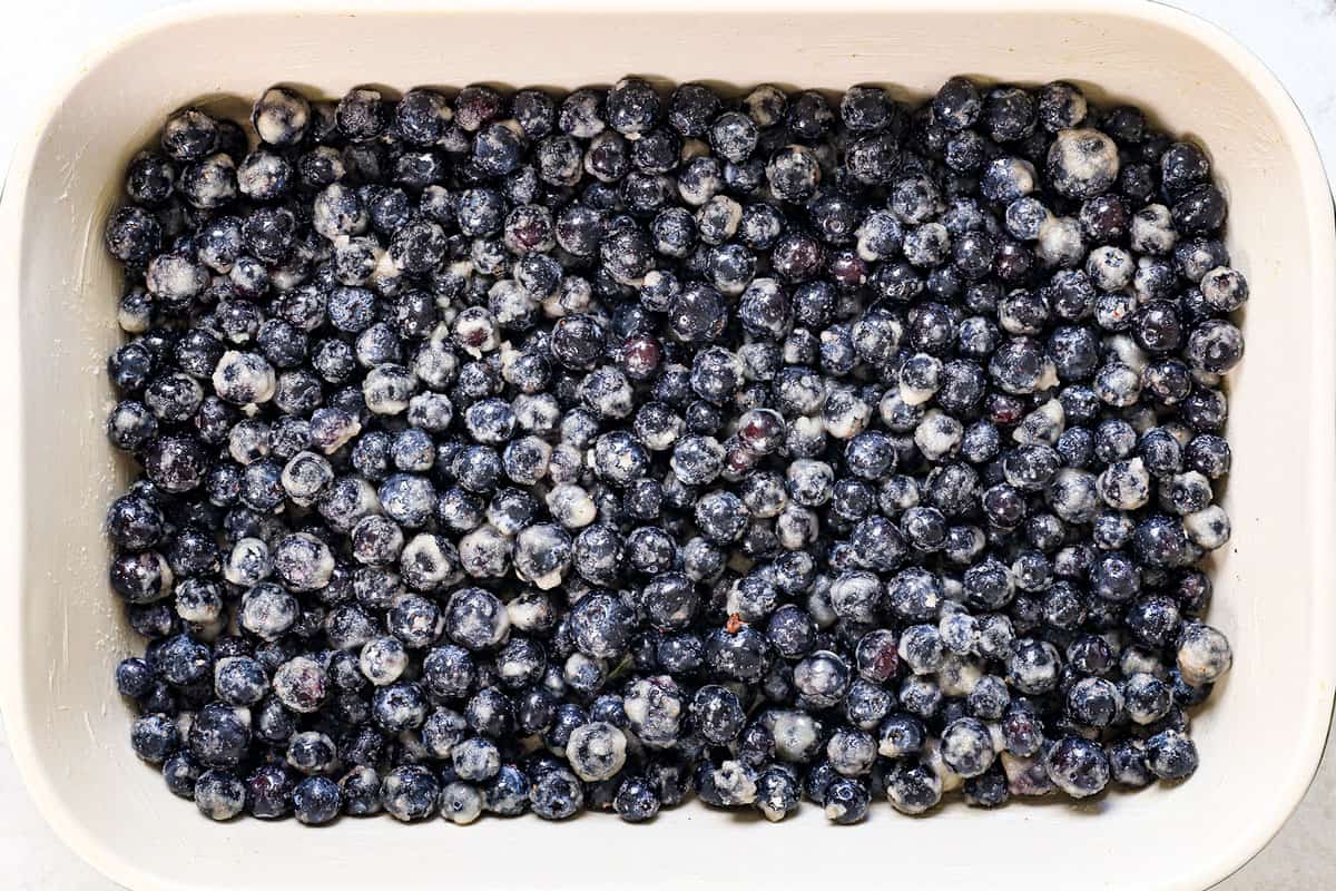 showing how to make a blueberry dump cake by adding the blueberries to a 9x13 baking dish