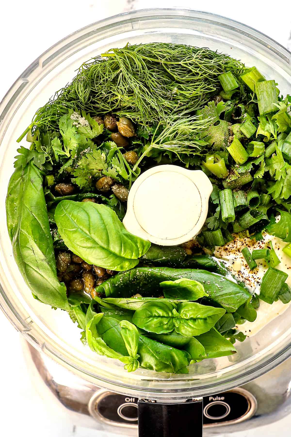 showing how to make green goddess dressing by adding parsley, basil, cilantro, green onions, chives, garlic, lemon juice, lemon zest, and Greek yogurt to a food processor