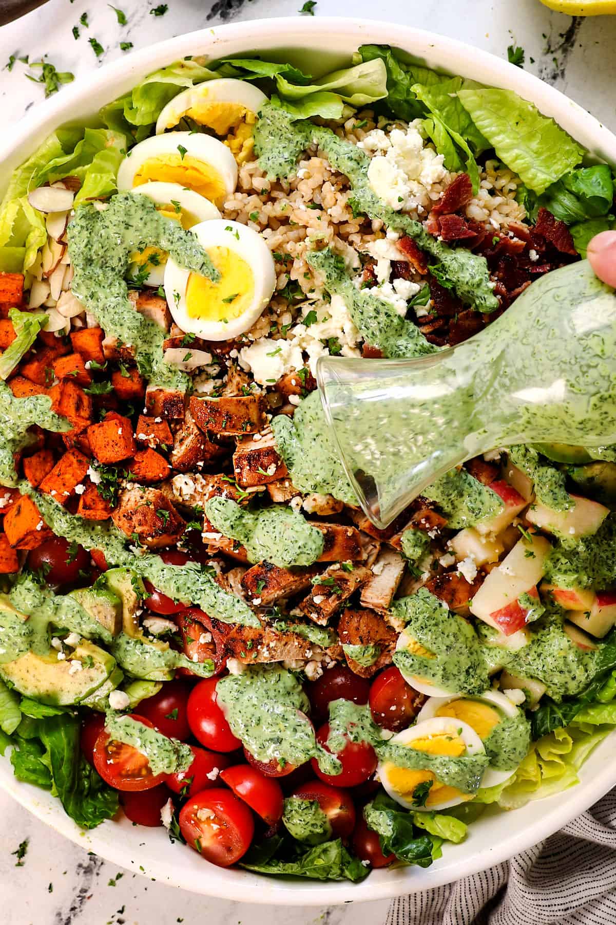 showing how to make green goddess salad by drizzling the dressing over the top of the salad