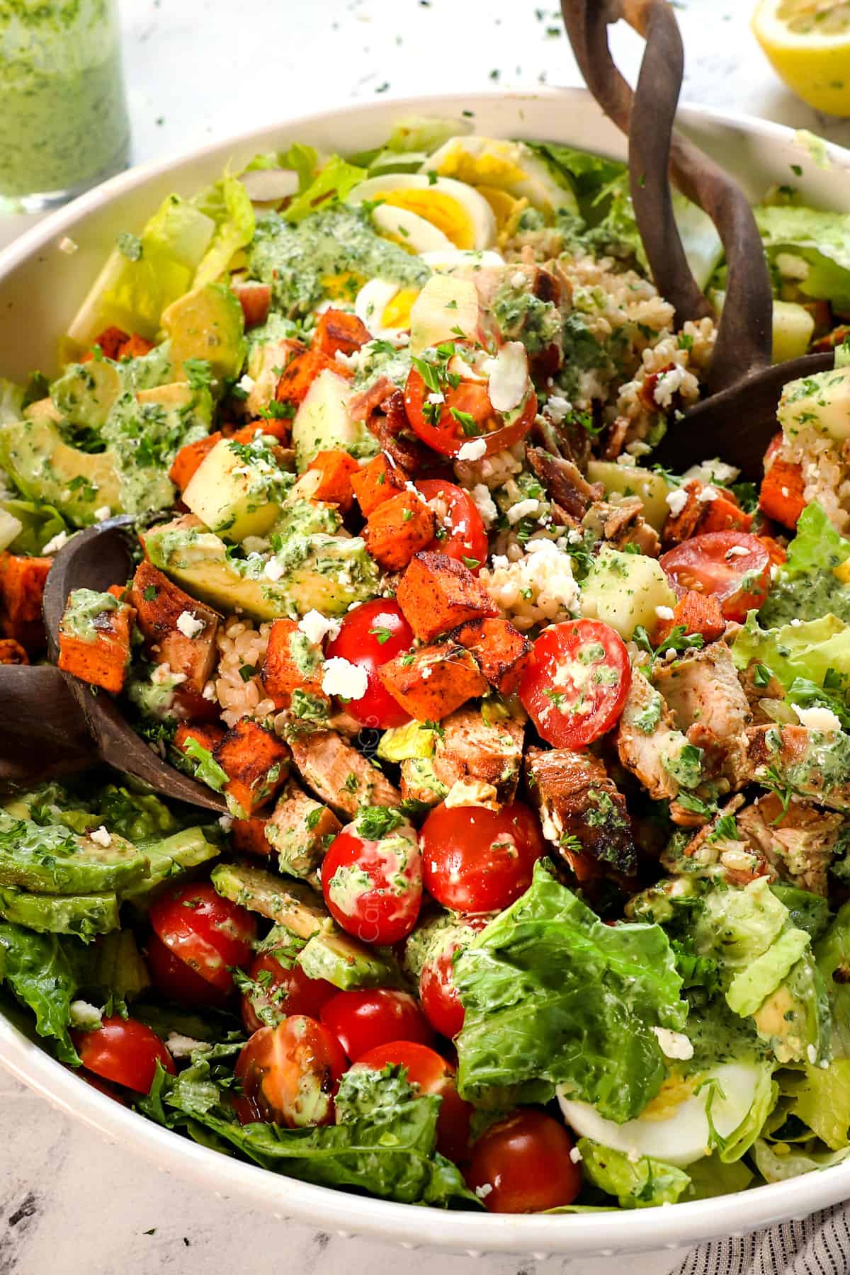 showing how to make green goddess salad by tossing the ingredients together with the dressing