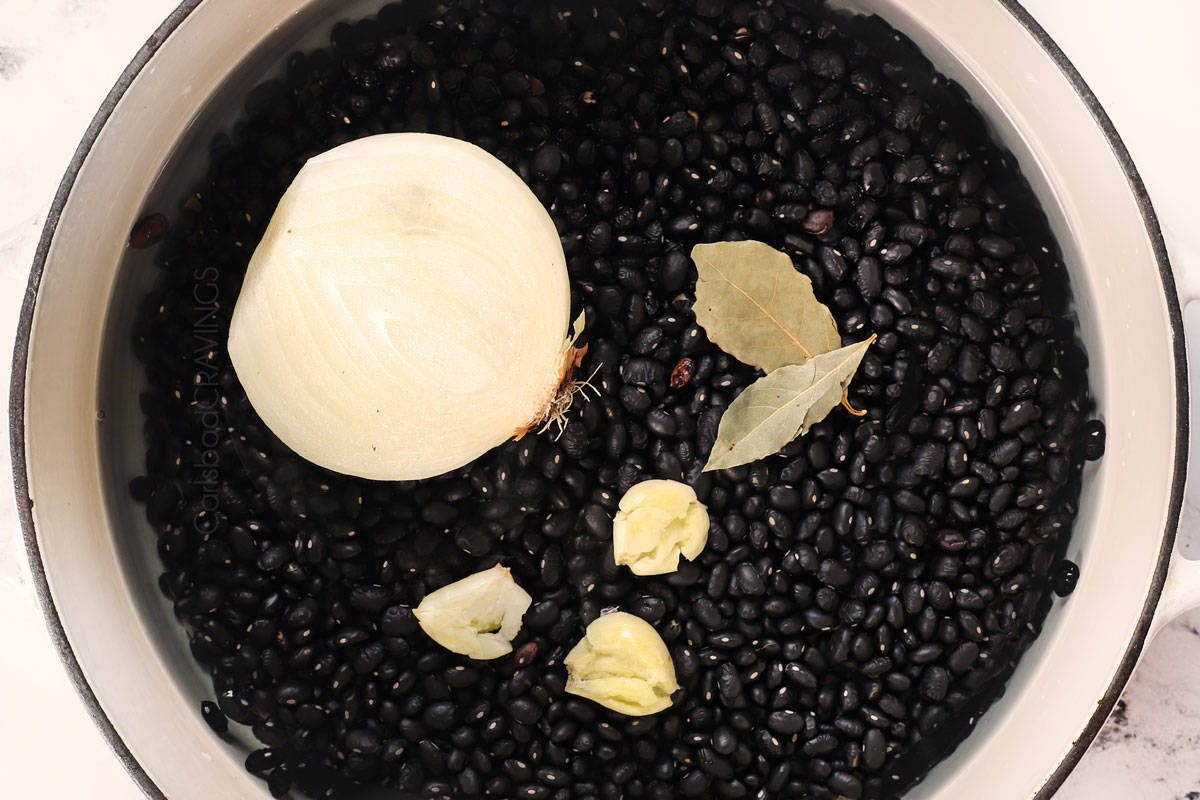 showing how to cook dried black beans by rinsing, then adding to the pot with onion, garlic and bay leaves