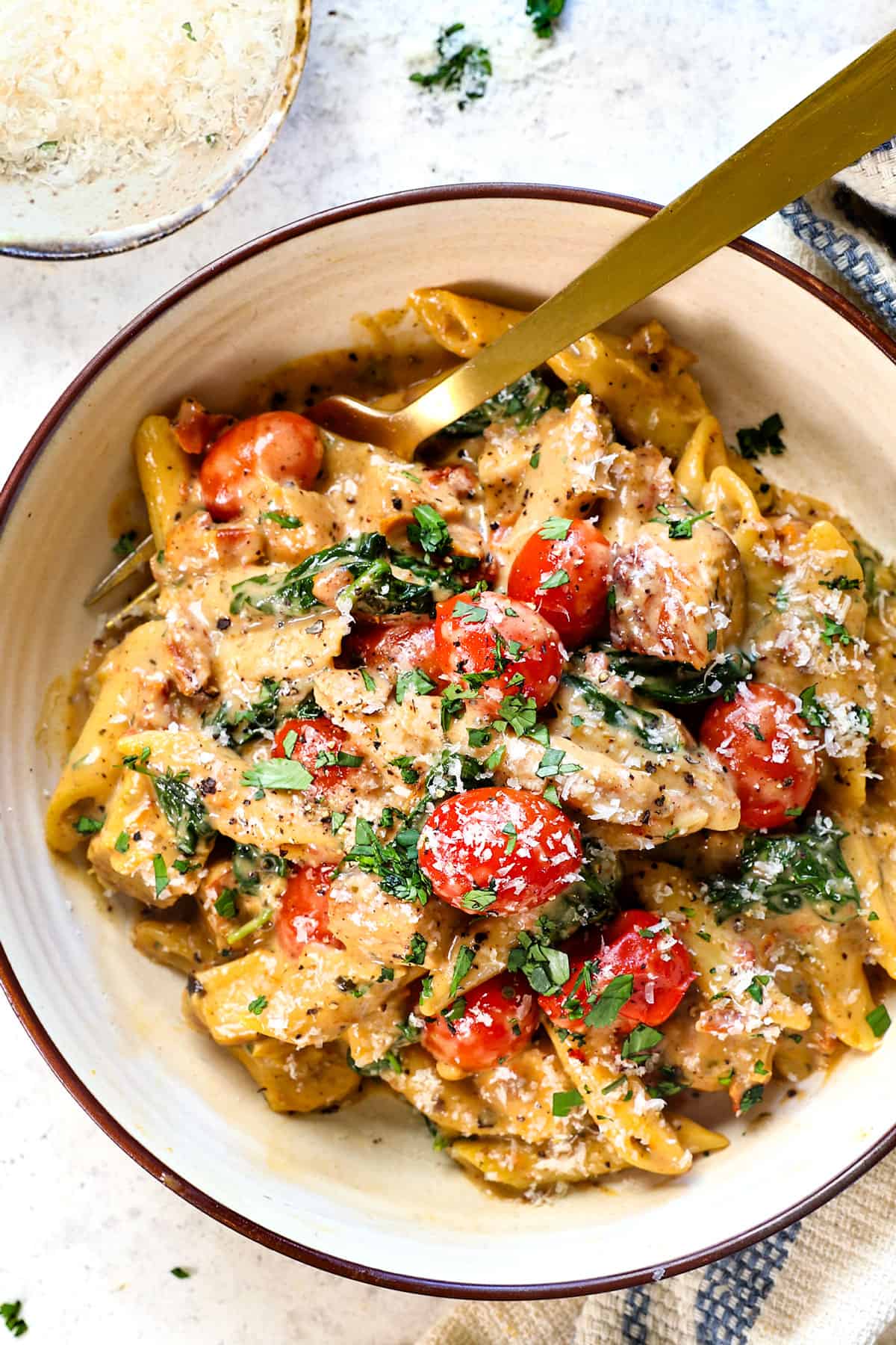 top view of serving creamy chicken Tuscan pasta in a bowl garnished by Parmesan and parsley