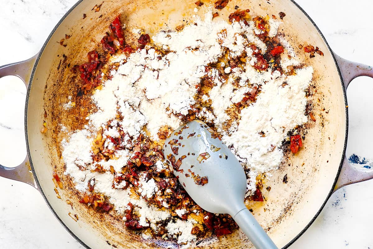 showing how to make Tuscan Chicken Pasta by sprinkling flour over the aromatics and cooking for one minute