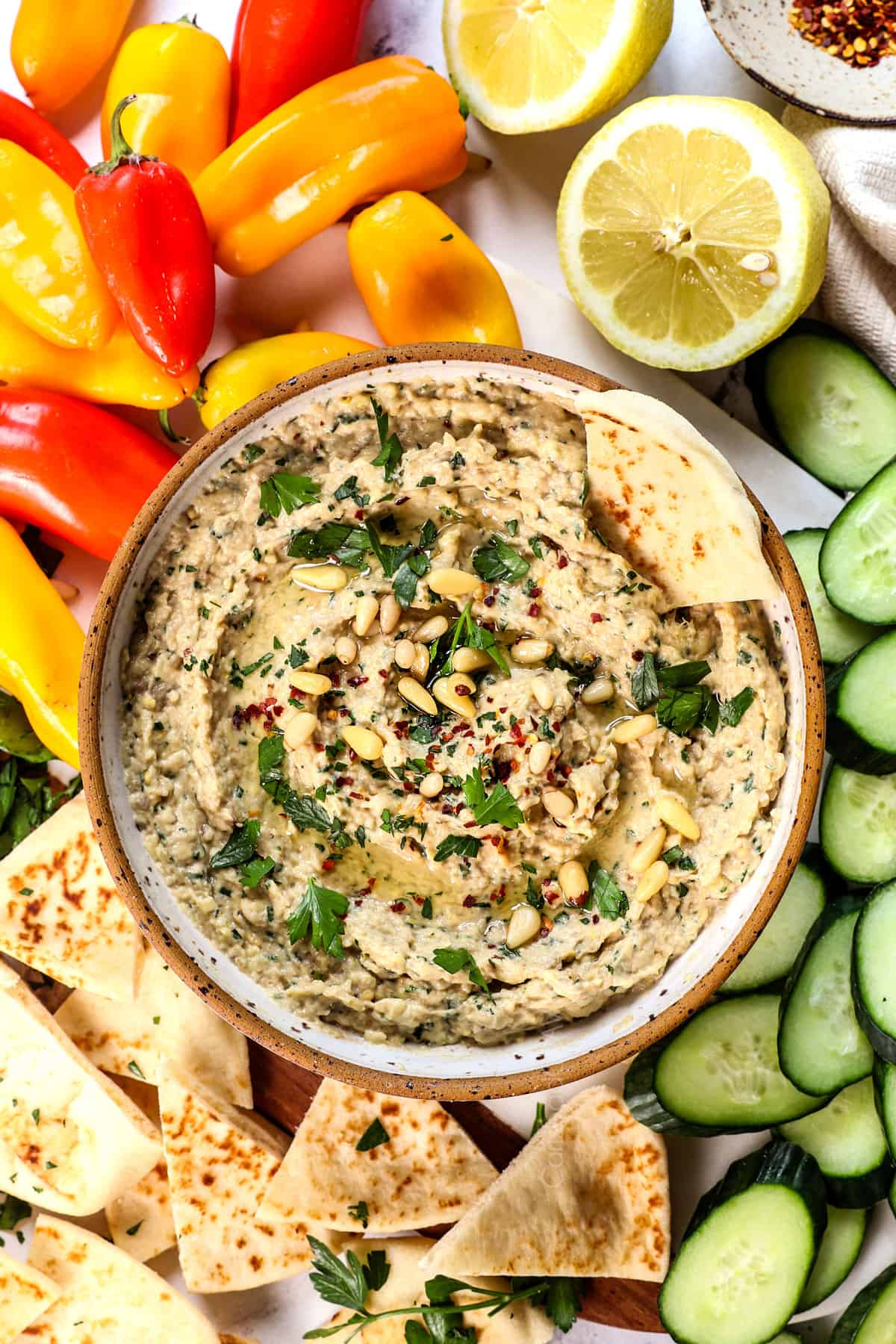 showing how to serve baba ghanouj with a top view of it in a bowl with parsley, pine nuts and paprika, drizzled with olive oil