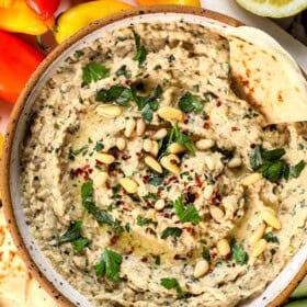 showing how to serve baba ghanouj with a top view of it in a bowl with parsley, pine nuts and paprika, drizzled with olive oil