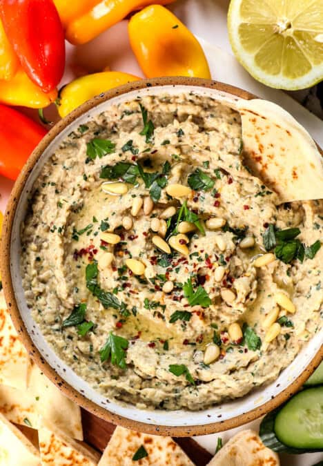 showing how to serve baba ghanouj with a top view of it in a bowl with parsley, pine nuts and paprika, drizzled with olive oil