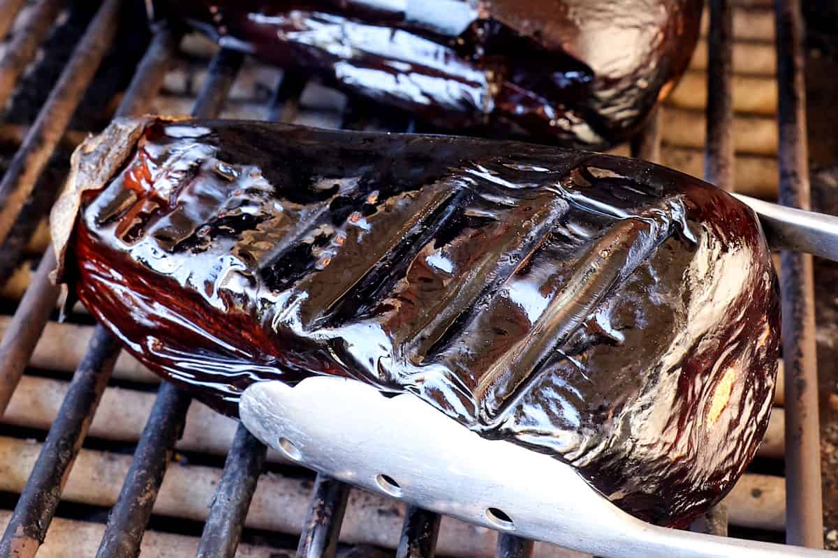 showing how to make baba ganoush by cooking the eggplant on the grill until it is soft and has collapsed 