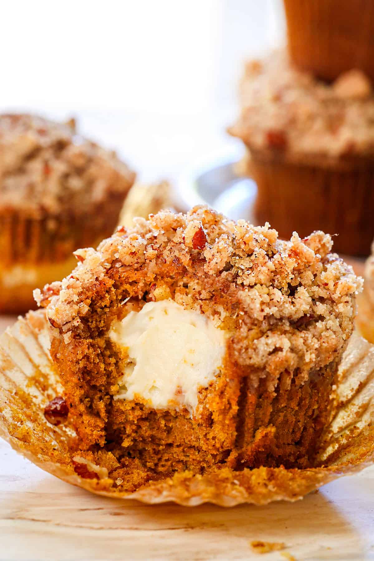 pumpkin cream cheese muffins with a bite taken out showing how creamy the cheesecake filling is