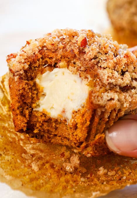 holding a pumpkin cream cheese muffin with a bite taken out showing how creamy the cheesecake center is with a crunchy streusel topping