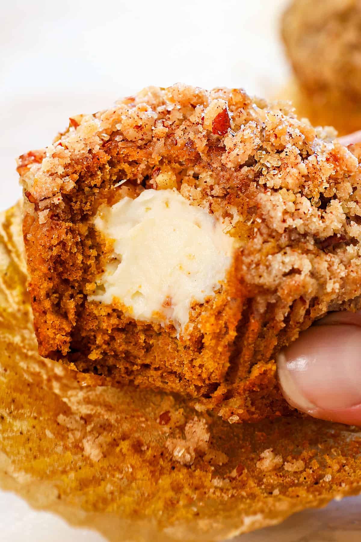 holding a pumpkin cream cheese muffin with a bite taken out showing how creamy the cheesecake center is with a crunchy streusel topping