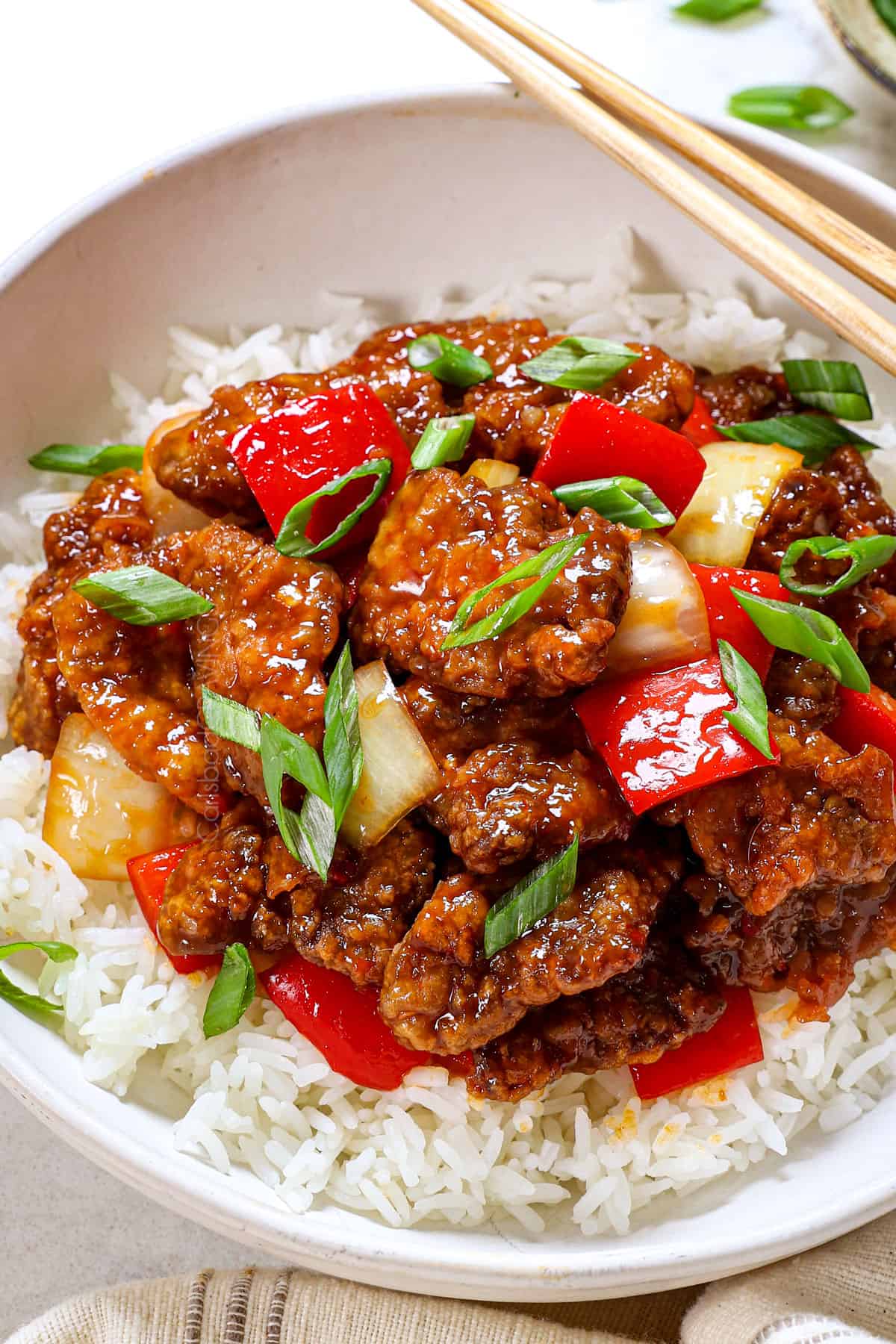 showing how to serve Beijing beef in a bowl over rice with green onions and chopsticks