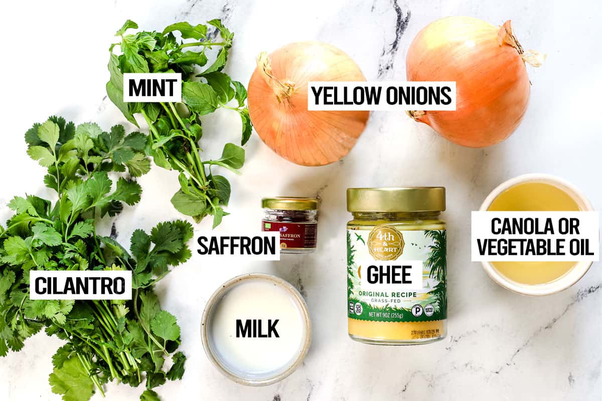 showing layering ingredients for biryani recipe: cilantro, mint, yellow onions, ghee, saffron, milk and oil  