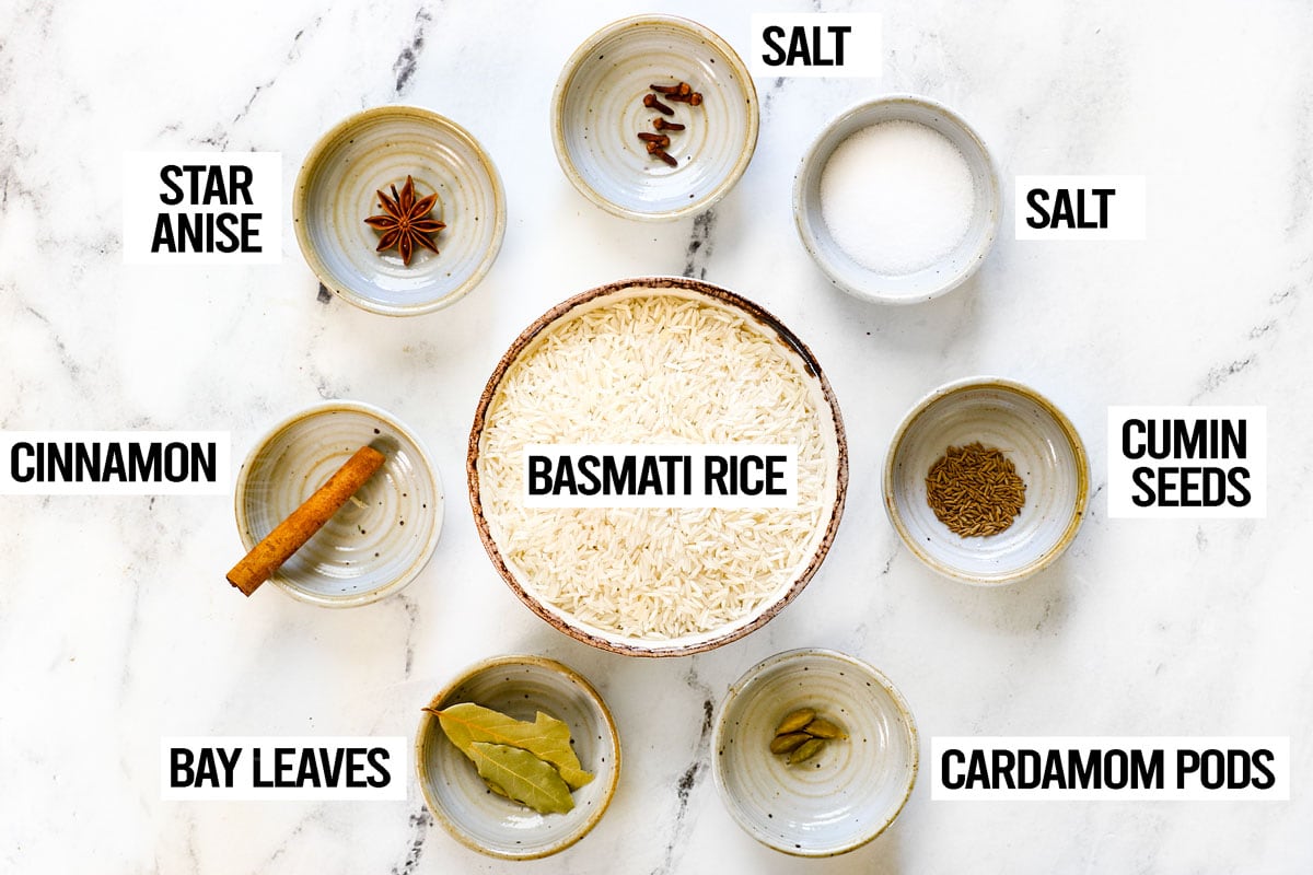 showing rice ingredients for biryani: basmati rice, bay leaves, cinnamon, star anise, cumin seeds, cardamom pods and salt 