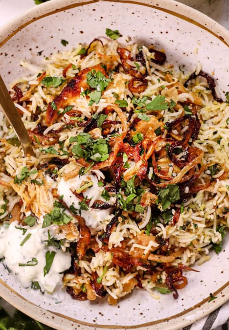 up close of serving biryani recipe garnished with mint, cilantro, served with raita