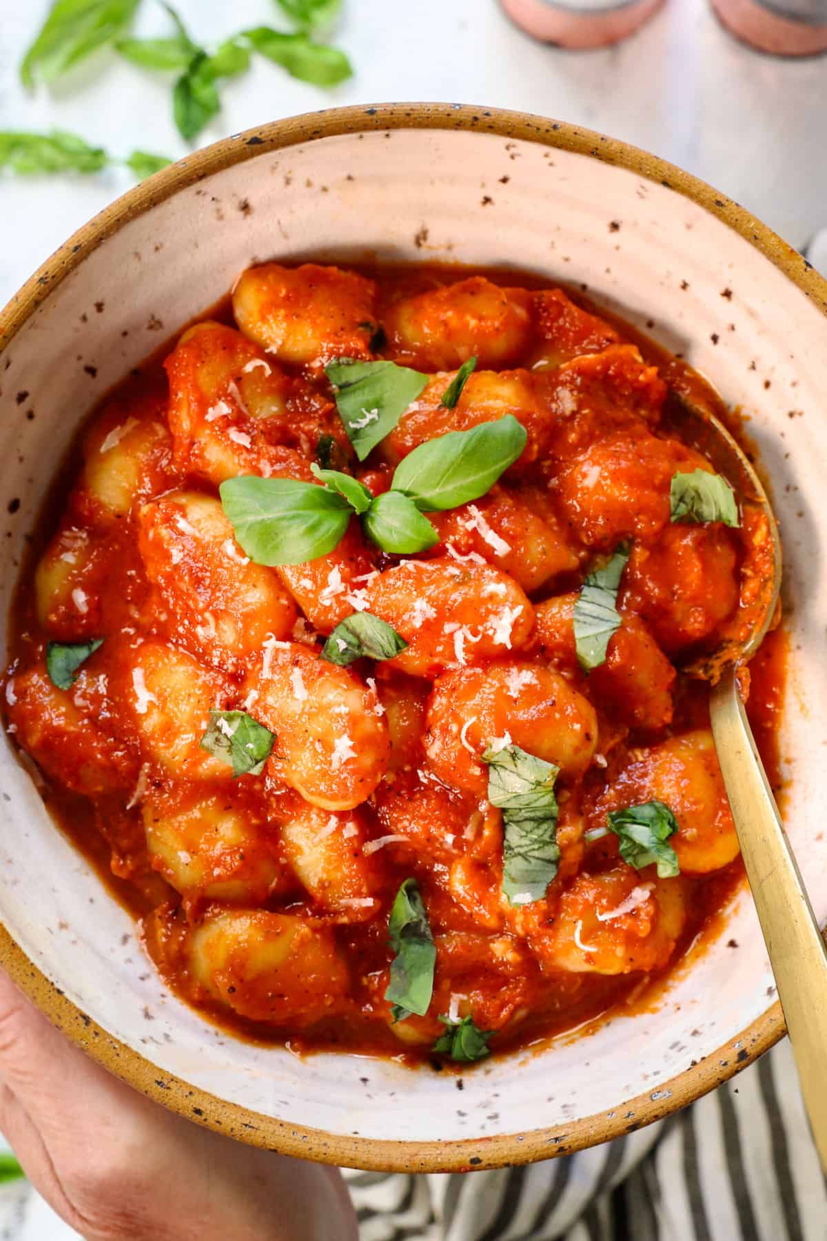 two hands holding a bowl of gnocchi alla sorrentina in a bowl garnished with fresh basil and Parmesan