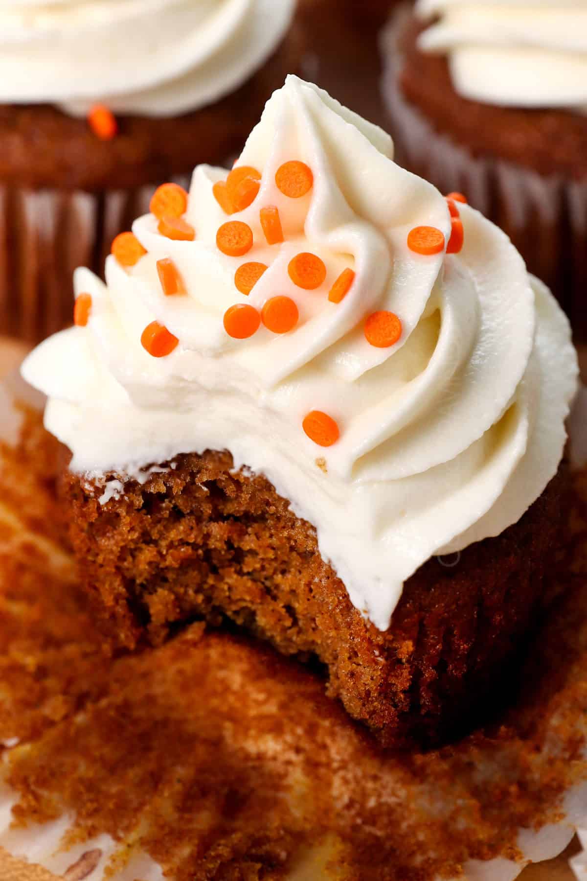 up close of pumpkin cupcakes with cream cheese frosting with a bite taken out of it, showing how soft, tender and moist it is